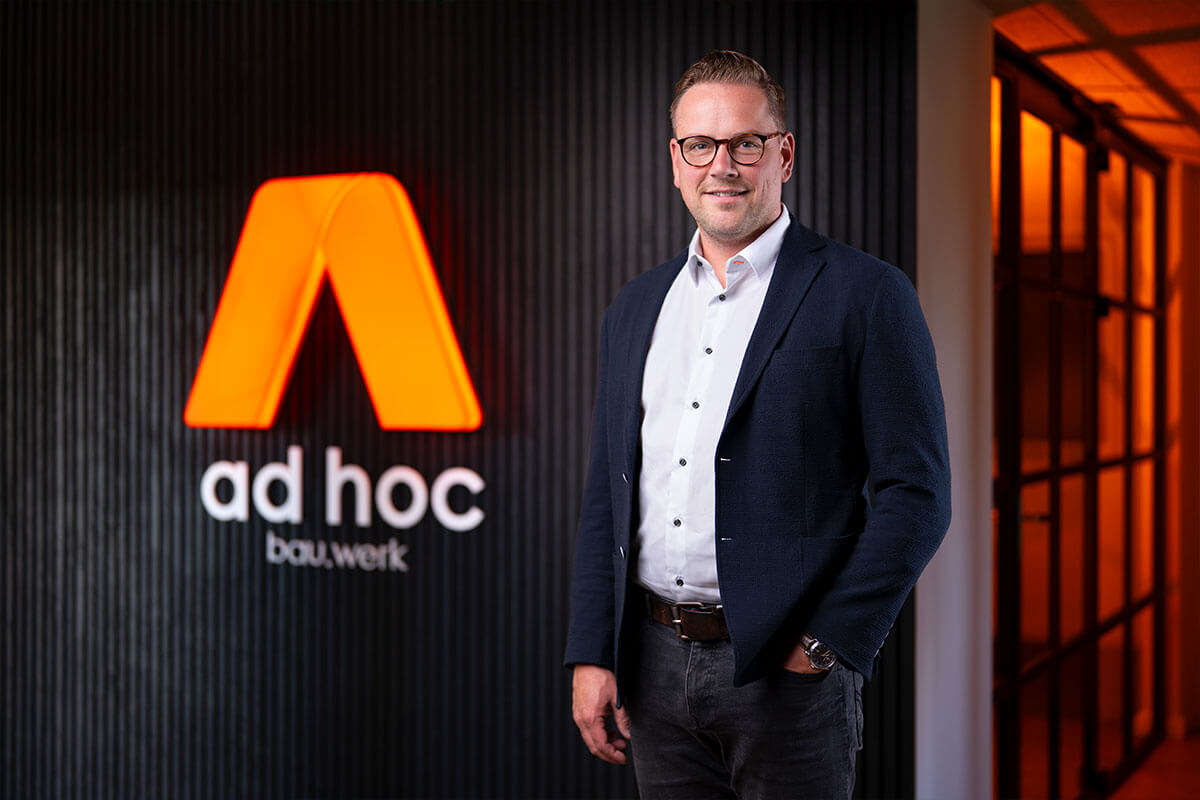 Porträt vor dem orange leuchtenden Schriftzug ad hoc bau.werk