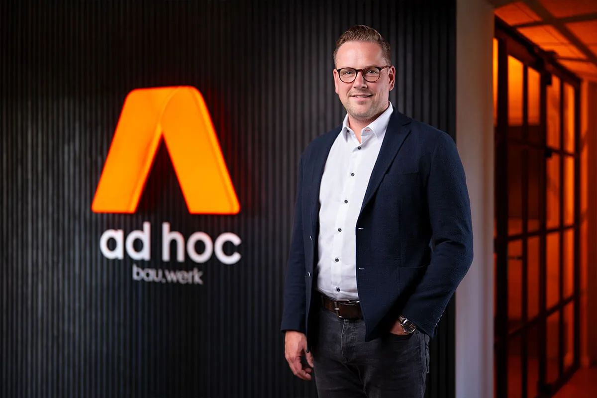 Geschäftsführer von ad hoc bau.werk vor dem orange leuchtenden Firmenlogo