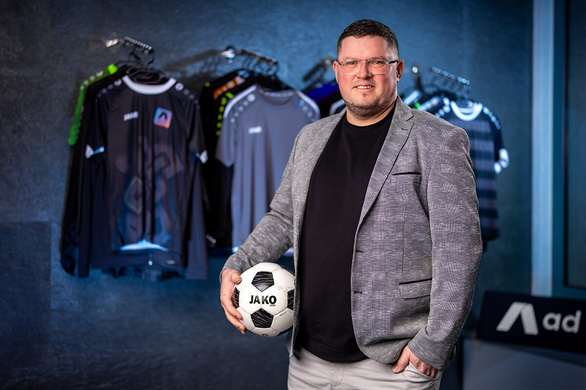 Porträt mit Fußball vor einer Wand mit Sporttrikots
