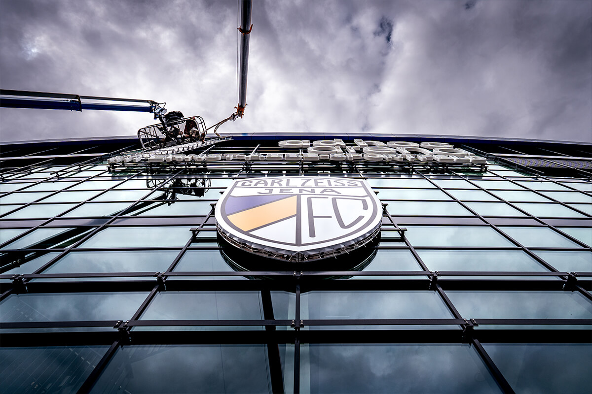 Montage des Vereinswappens an der Glasfassade des Stadions