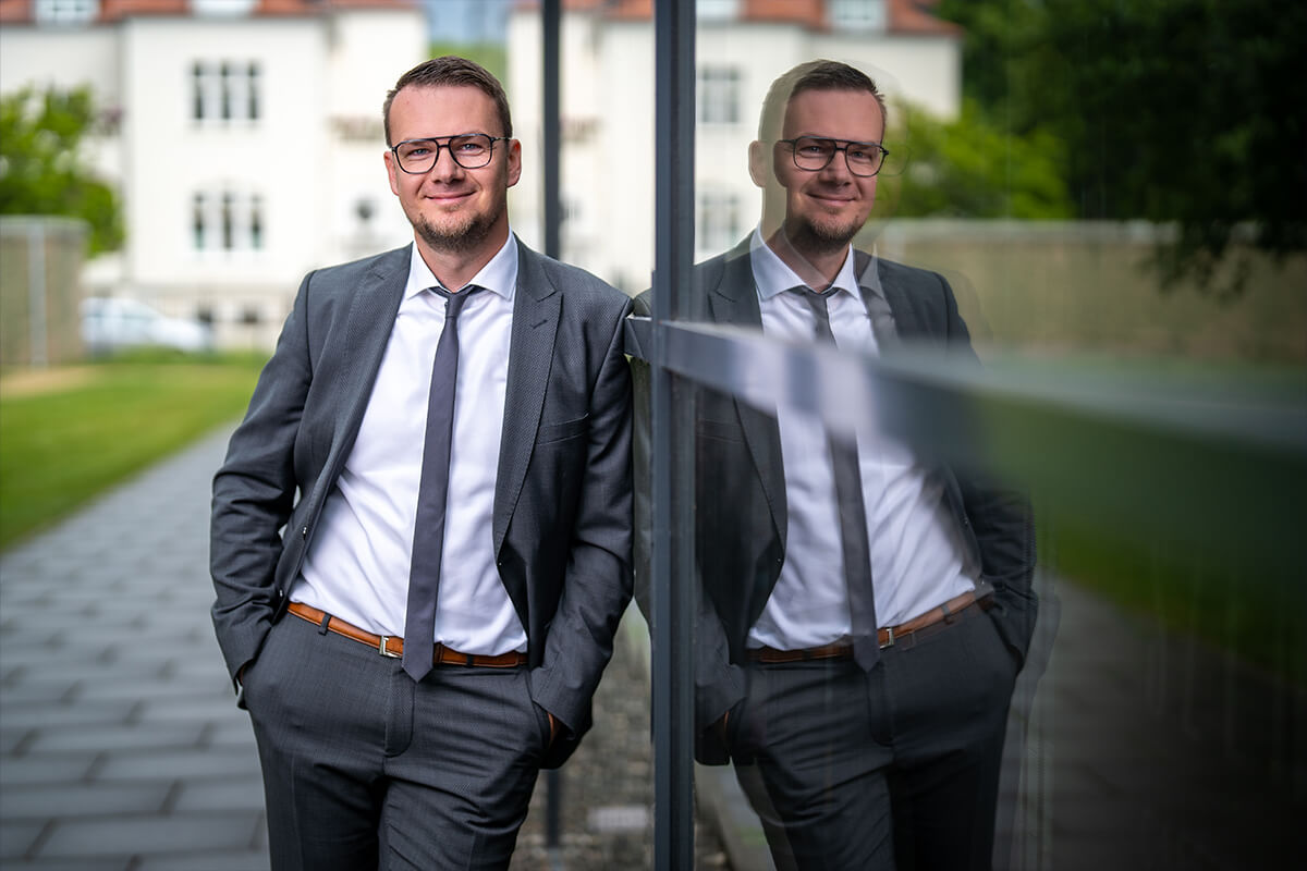 Porträt an einer Glasfassade mit Spiegelung, dahinter das Bürogebäude