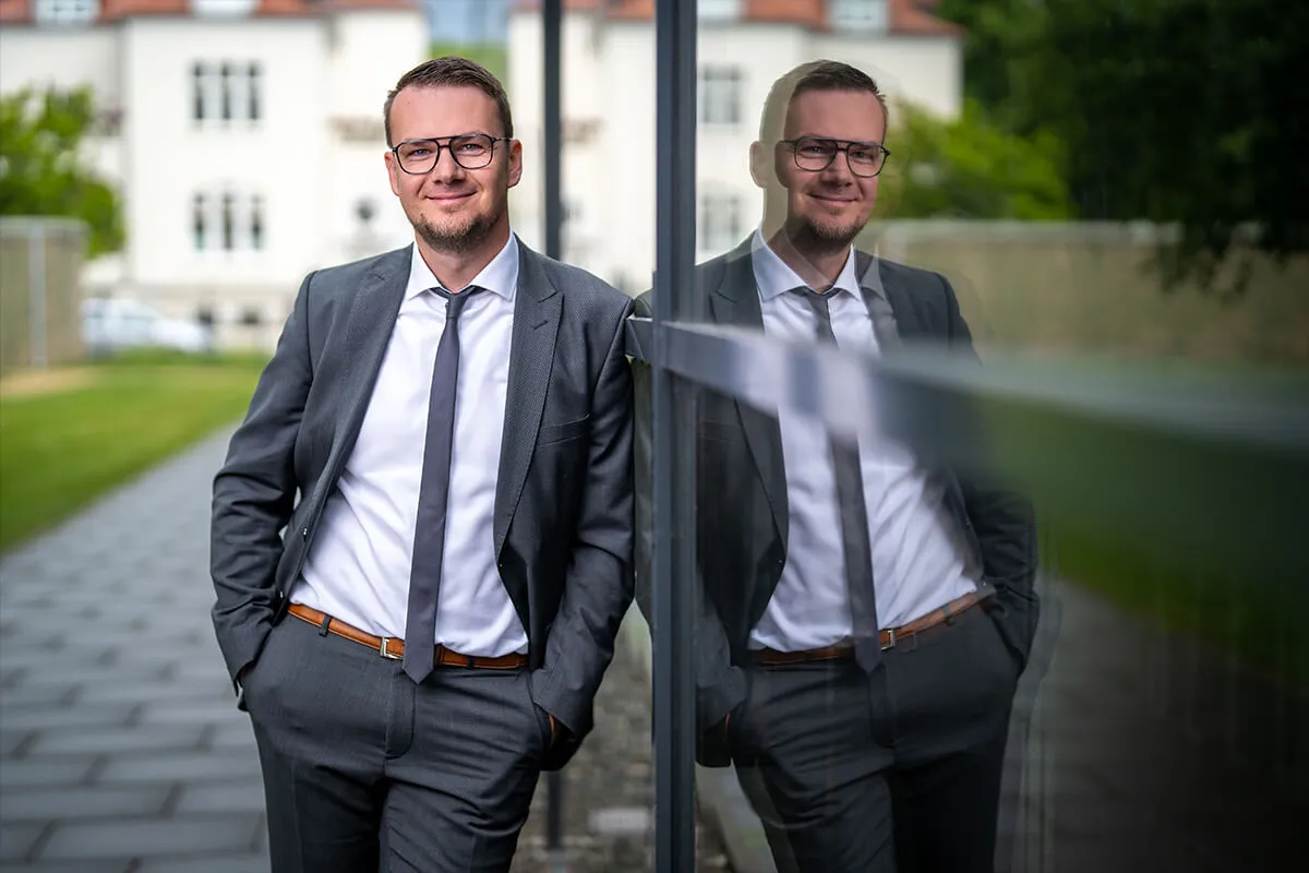 Business-Porträt eines Mitarbeiters im Anzug mit Spiegelung in der Glasfassade