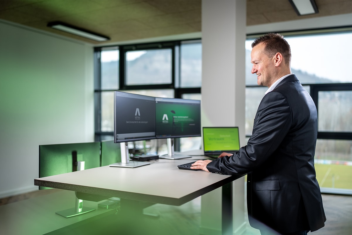 Am Stehtisch vor zwei Monitoren, auf dem Laptop die Website des ad hoc Versicherungsdienstes