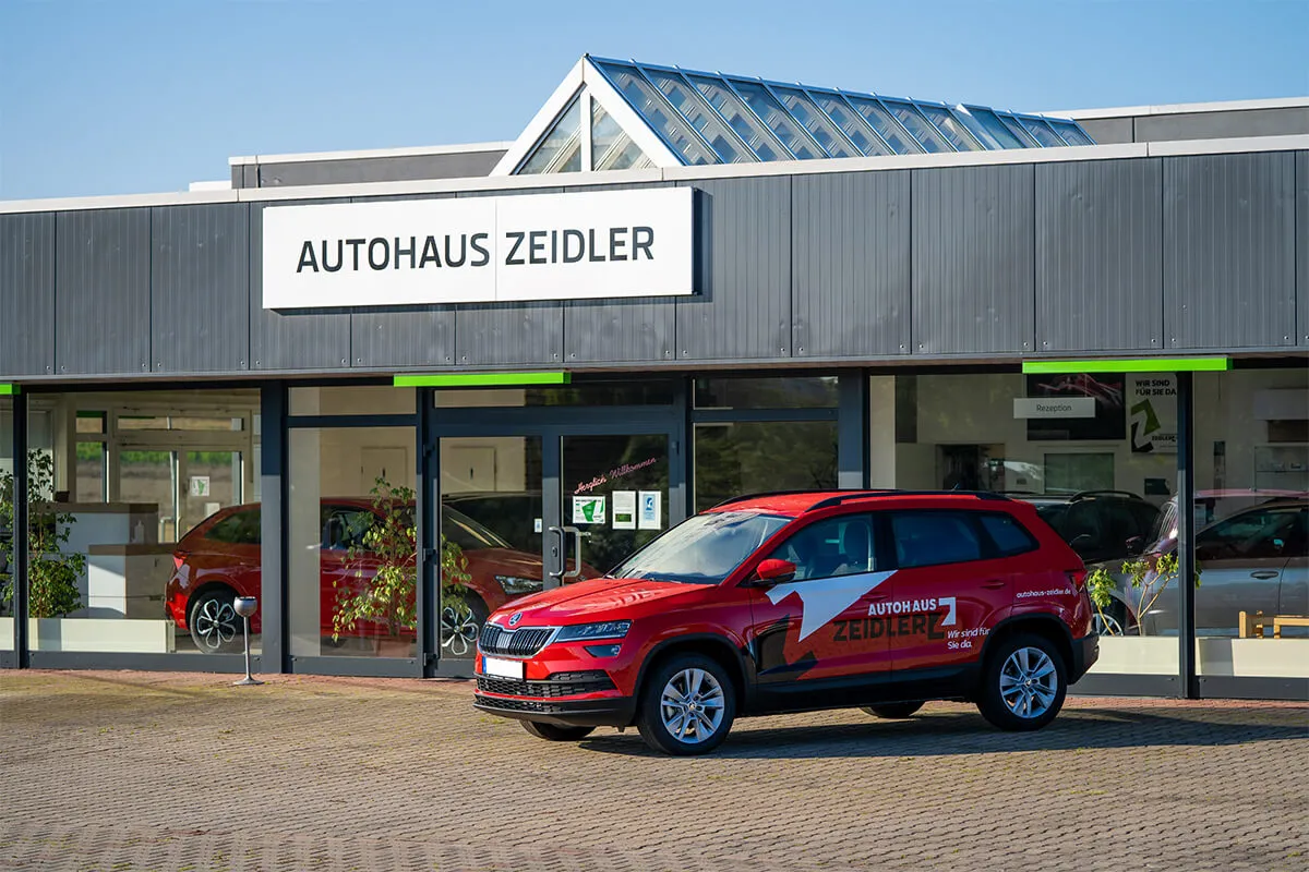 Firmenschild „Autohaus Zeidler" über dem Eingang mit rotem Servicefahrzeug