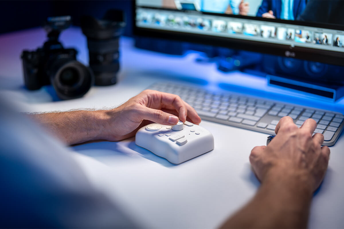 Hand am Bedienpult bei der Bildbearbeitung, im Hintergrund die Bildauswahl auf dem Monitor