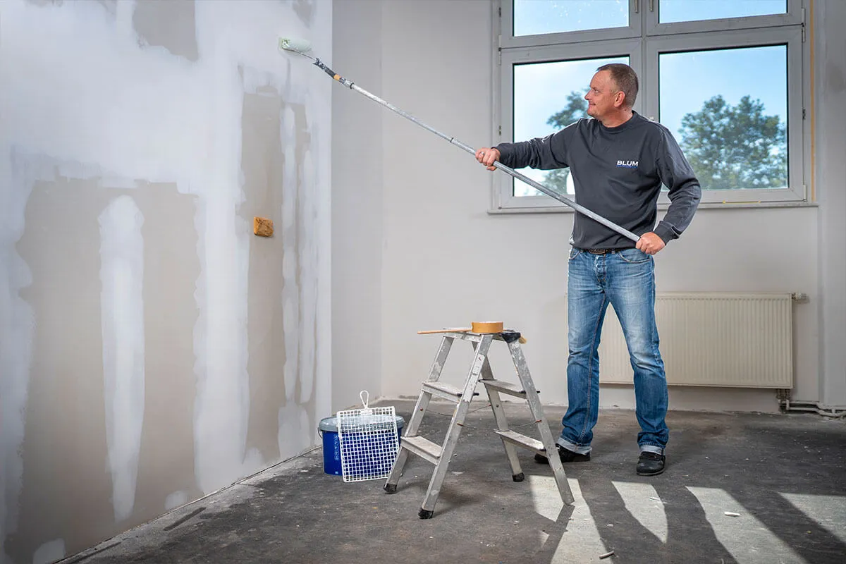 Mitarbeiter streicht eine Wand mit der Rolle am Teleskopstiel