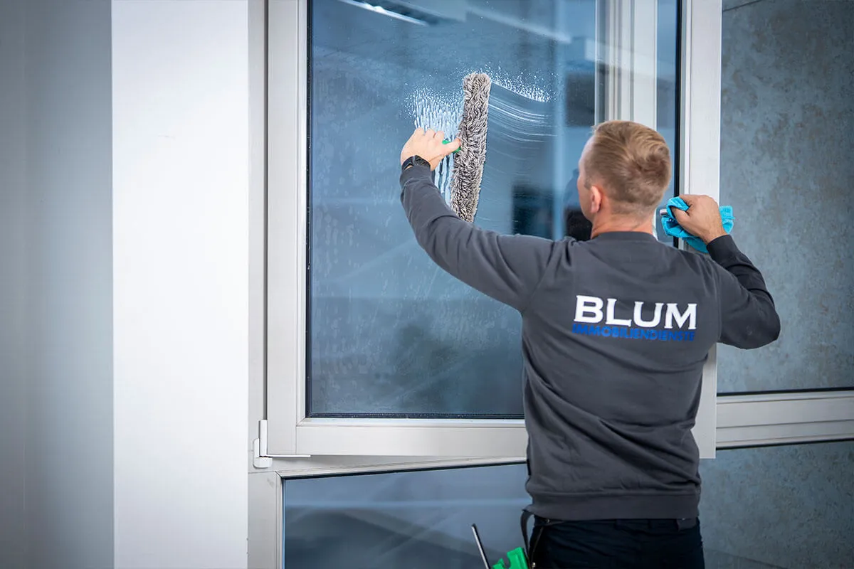 Mitarbeiter reinigt ein Fenster mit dem Abzieher