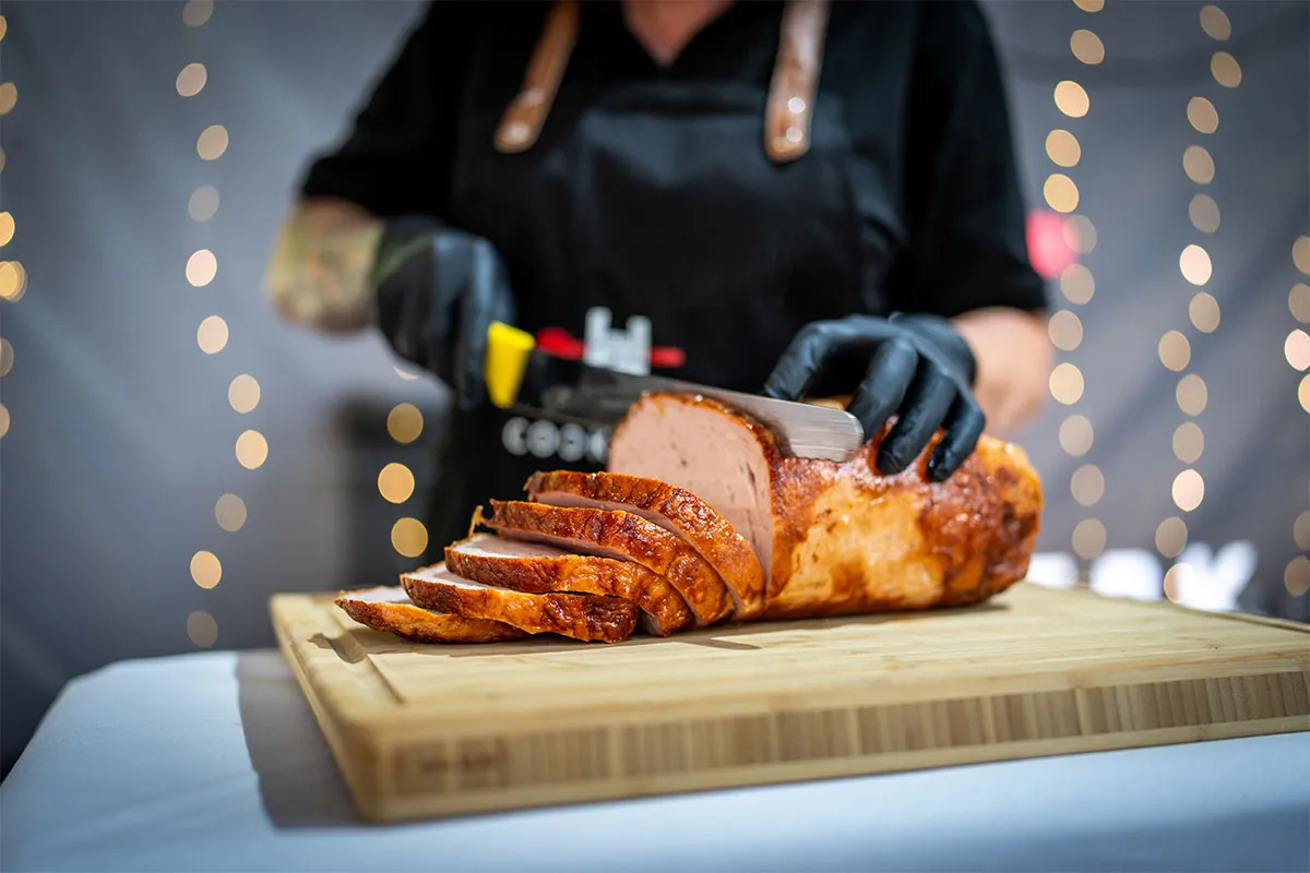 Küchenmitarbeiterin schneidet einen Braten am Cateringstand von CookWerk auf