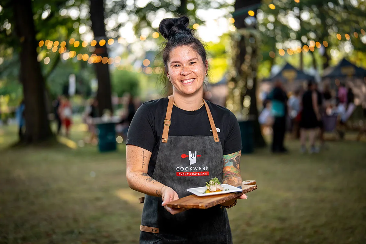 Küchenmitarbeiterin von CookWerk präsentiert ein angerichtetes Gericht auf dem Sommerfest
