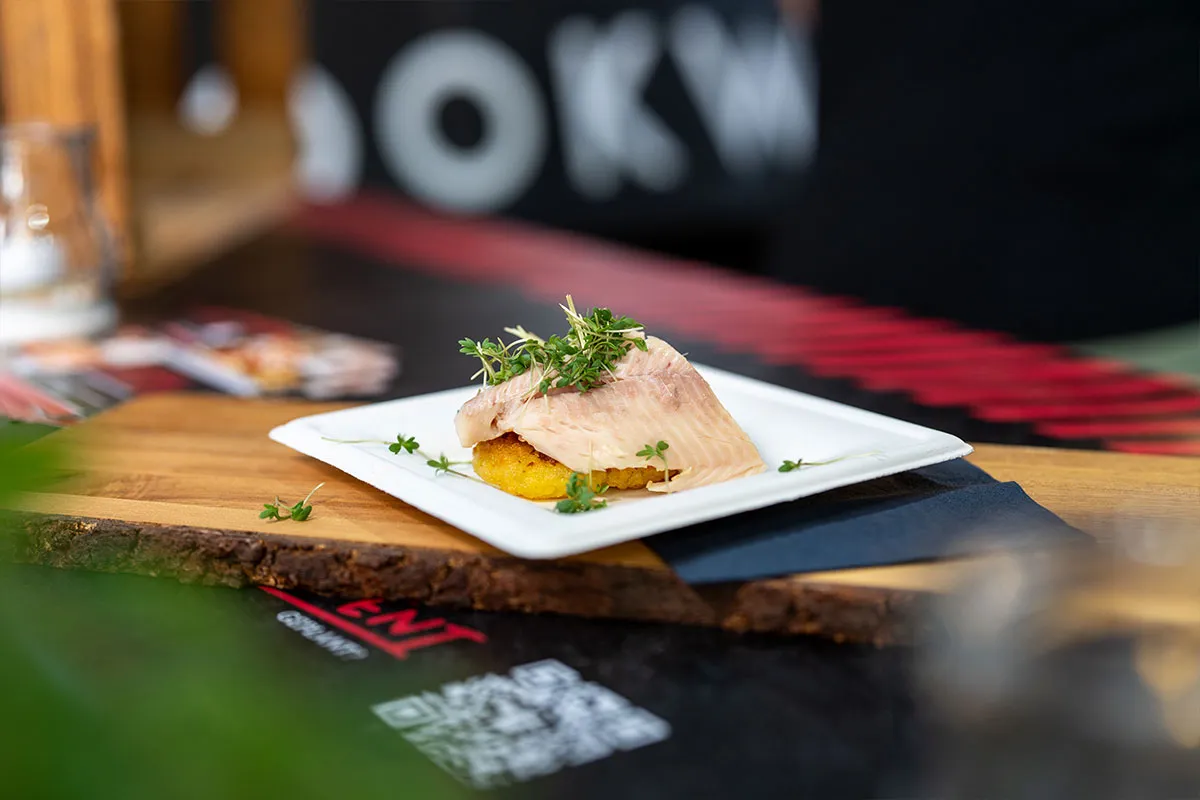 Angerichtetes Fischgericht auf weißem Teller vor der CookWerk-Bande