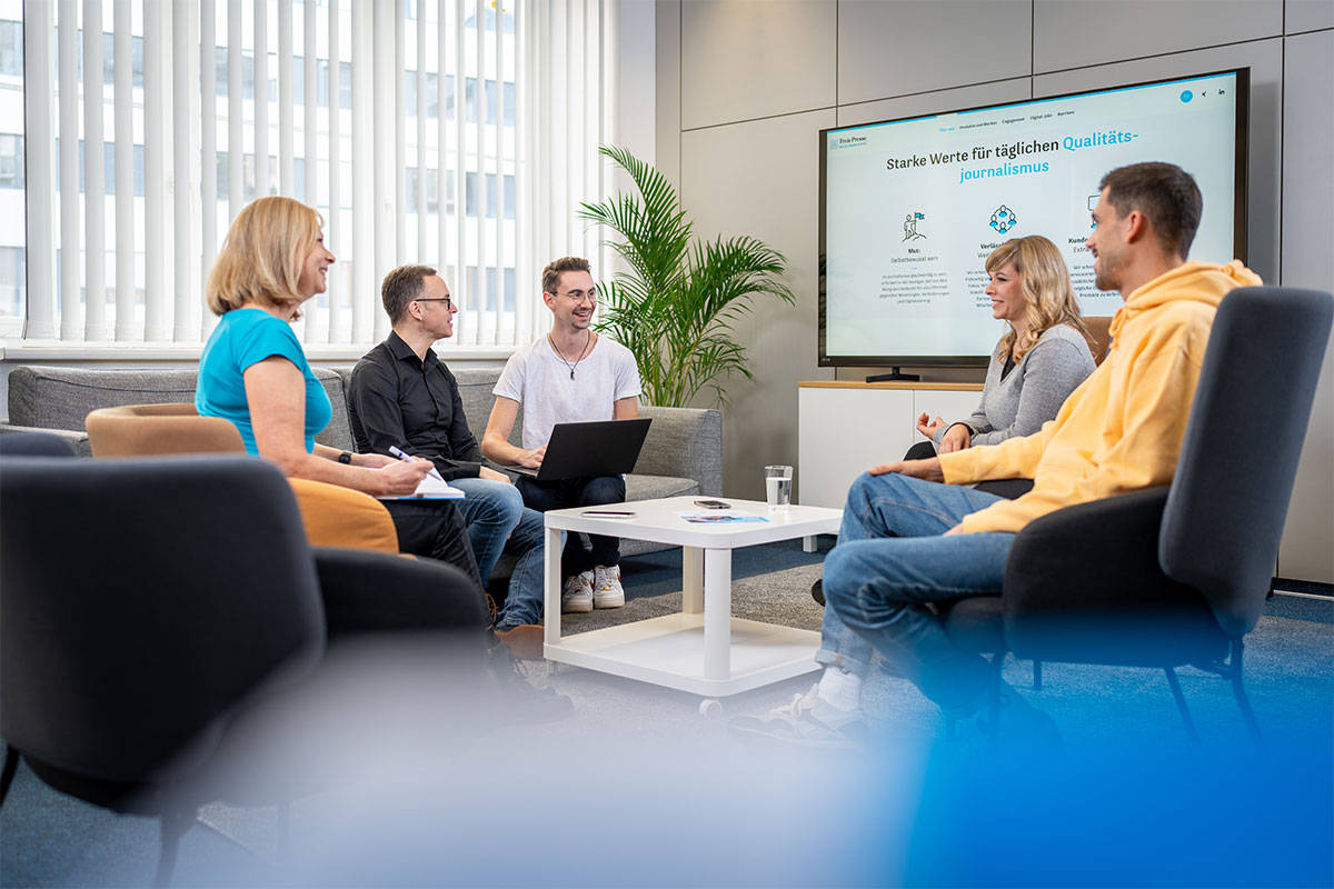 Teamrunde in der Sitzecke vor einem Bildschirm mit der Unternehmenswebsite