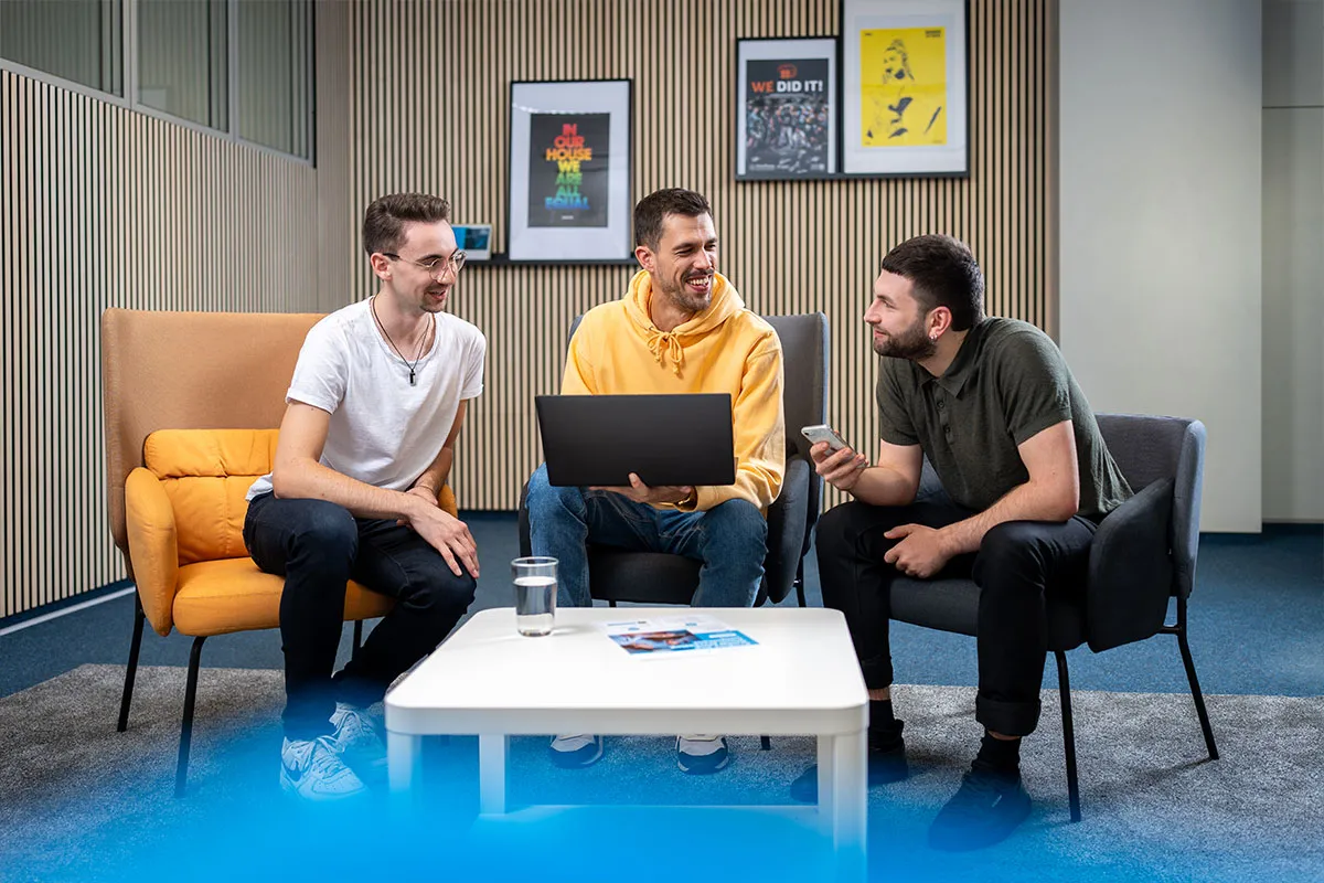 Drei junge Kollegen mit Laptop in der Sitzecke des Medienhauses