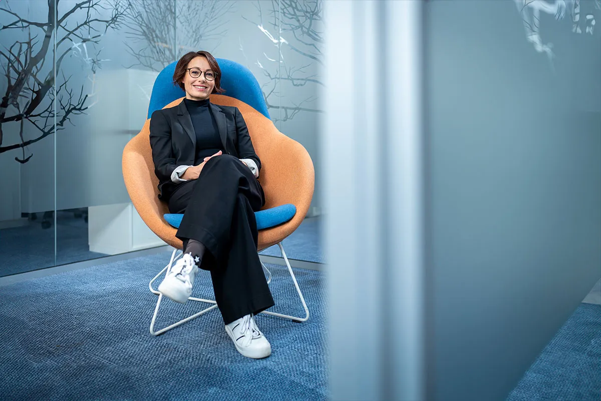 Business-Porträt einer Mitarbeiterin im Sessel vor blau beleuchteter Glasfassade