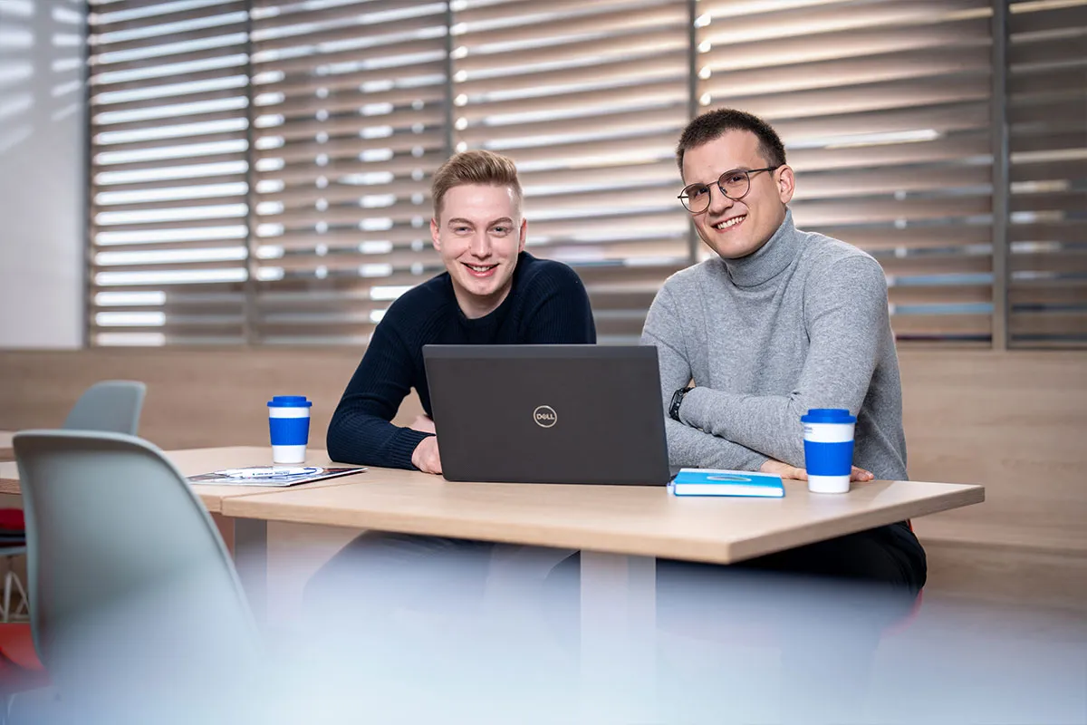 Zwei junge Mitarbeiter arbeiten gemeinsam am Laptop im Besprechungsraum