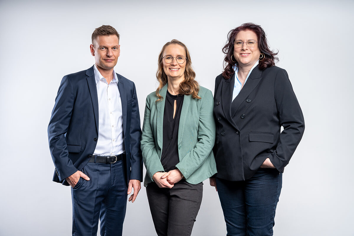 Studioporträt zu dritt, zwei Kolleginnen und ein Kollege nebeneinander