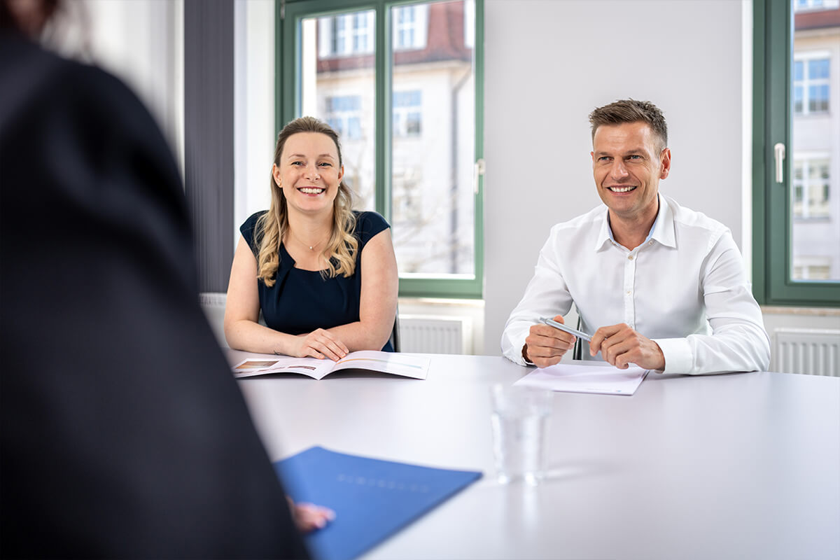 Beratungsgespräch am Besprechungstisch, zwei Mitarbeitende gegenüber dem Besuch