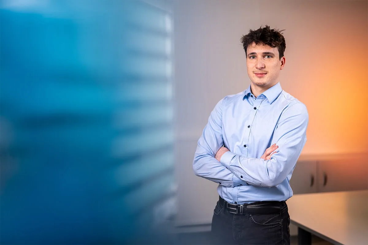 Porträt eines jungen Mitarbeiters mit verschränkten Armen im Büro