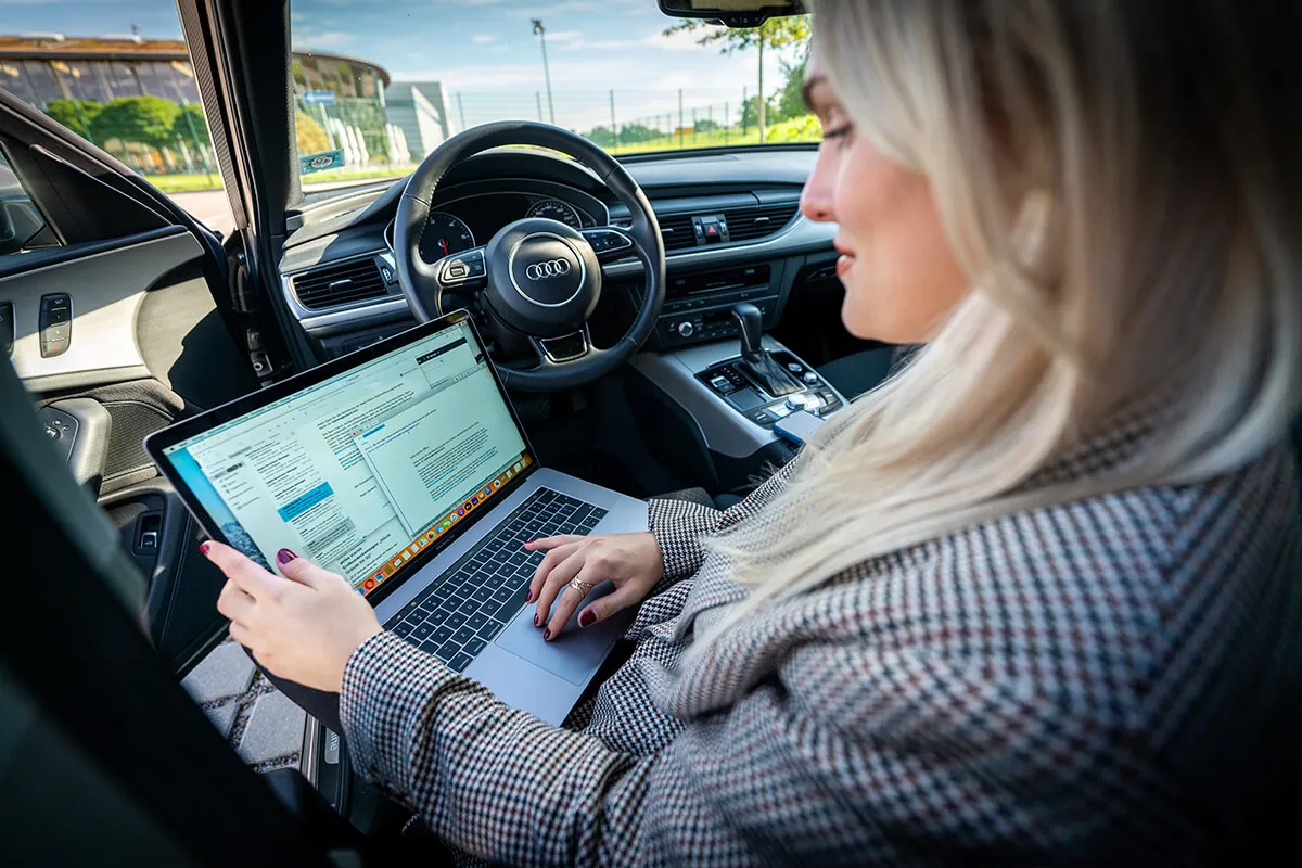 Mitarbeiterin arbeitet mit dem MacBook auf dem Beifahrersitz