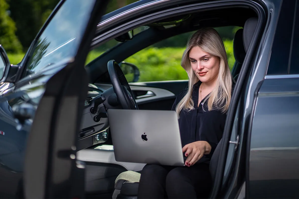 Mitarbeiterin mit MacBook in der geöffneten Autotür