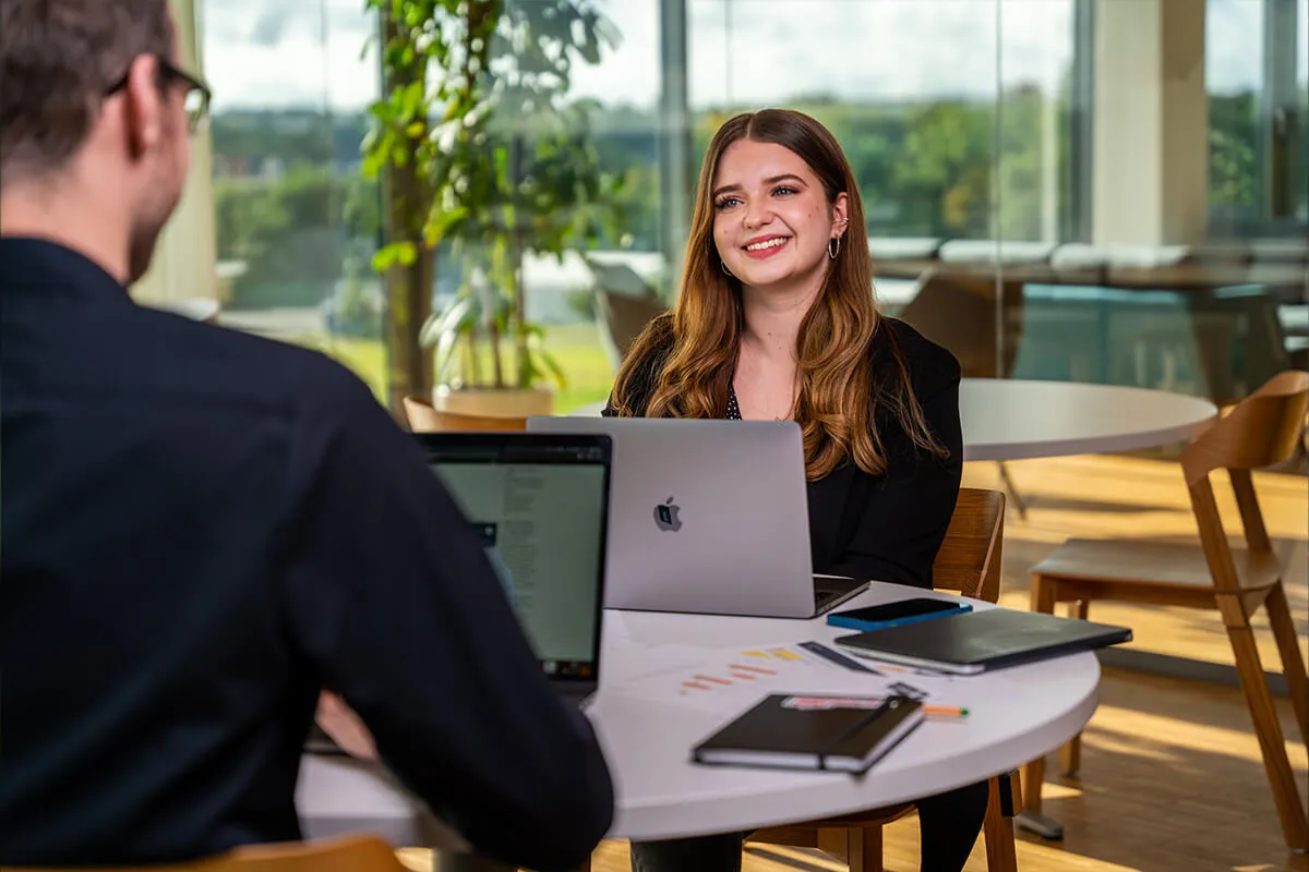 Zwei Kollegen mit MacBooks im lichtdurchfluteten Loungebereich
