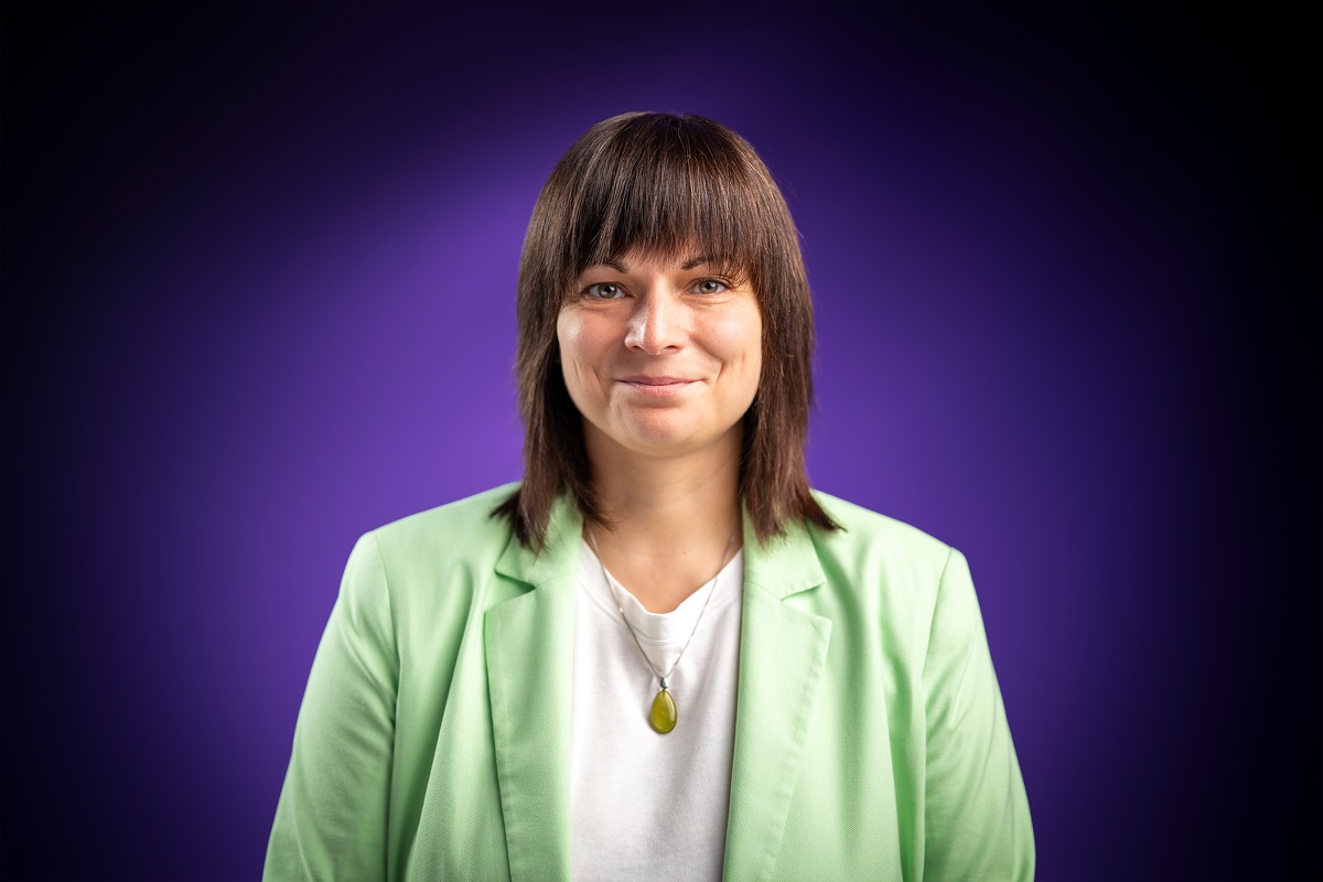 Anja Lauchart im hellgrünen Blazer, frontal vor einem lila Verlauf im Studio.
