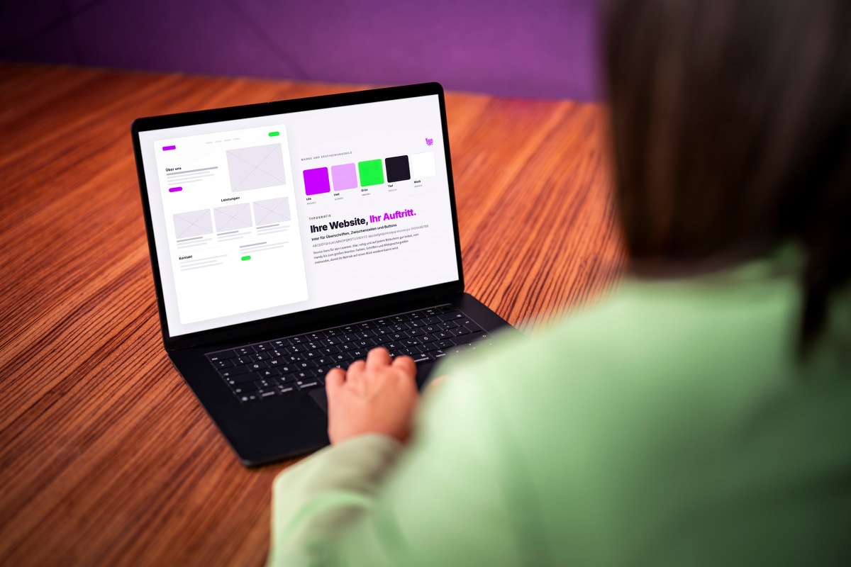 Blick über die Schulter von Anja Lauchart auf den Laptop mit der Seite „Ihre Website, Ihr Auftritt“ und lila und grünen Farbfeldern.