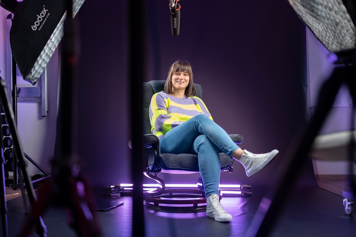 Anja Lauchart sitzt im gestreiften Pullover lachend in einem Sessel im Studio, umrahmt von Leuchten.