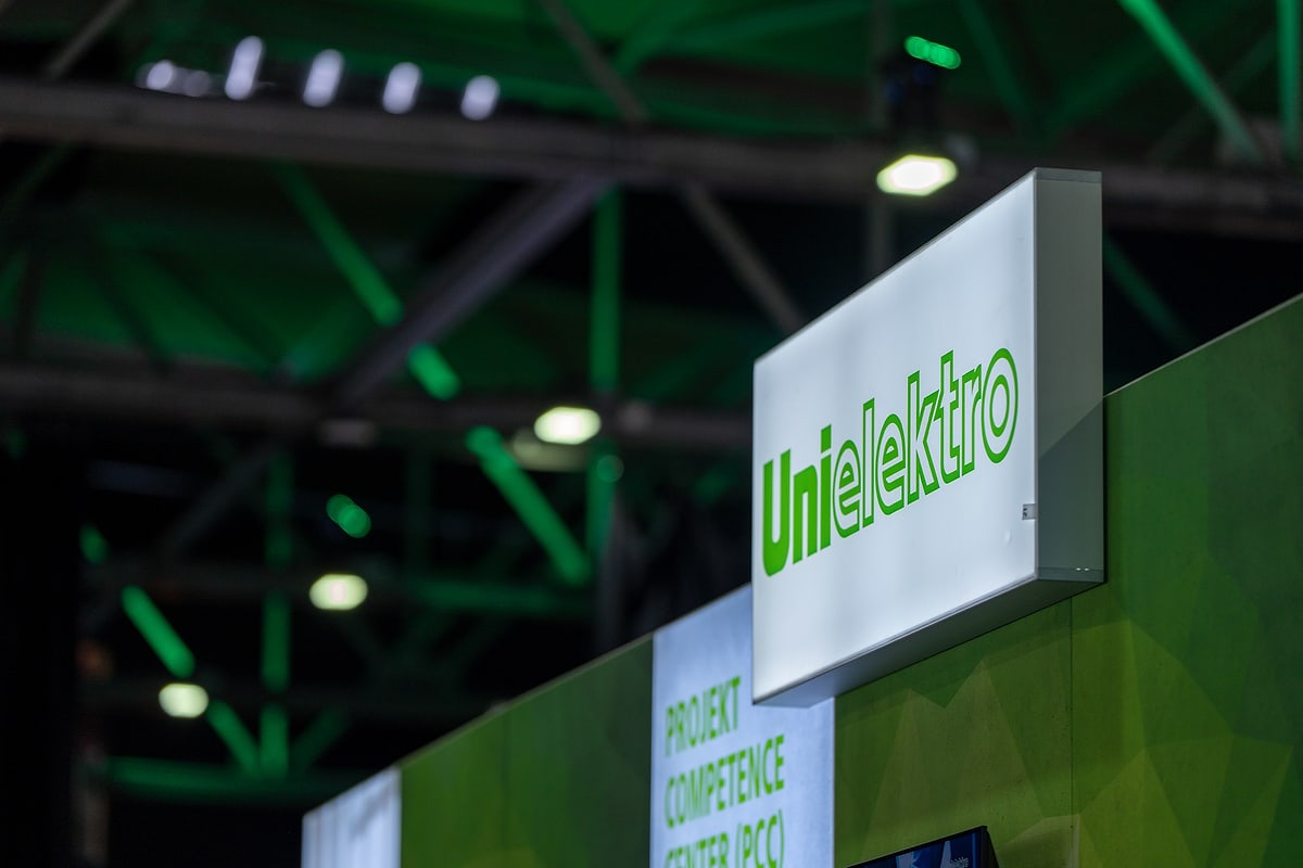 Standardbearbeitung derselben Aufnahme: Leuchtkasten mit UNI ELEKTRO Logo, die Hallendecke etwas aufgehellt