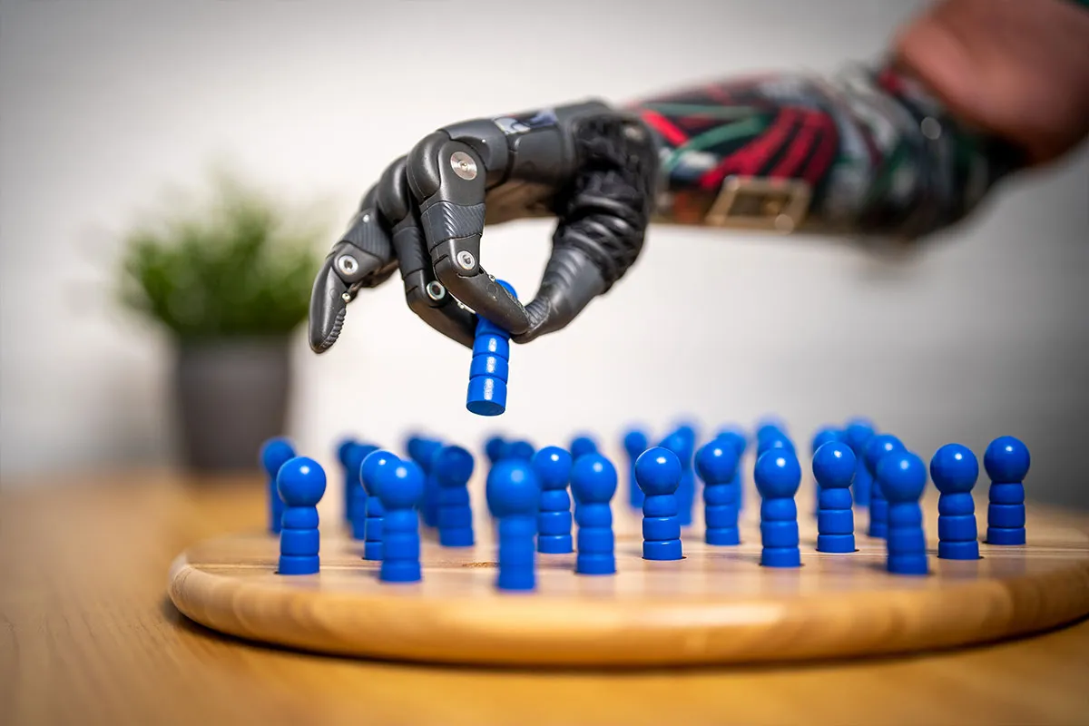 Bionische Handprothese greift einen blauen Spielstein von einem Holzbrett
