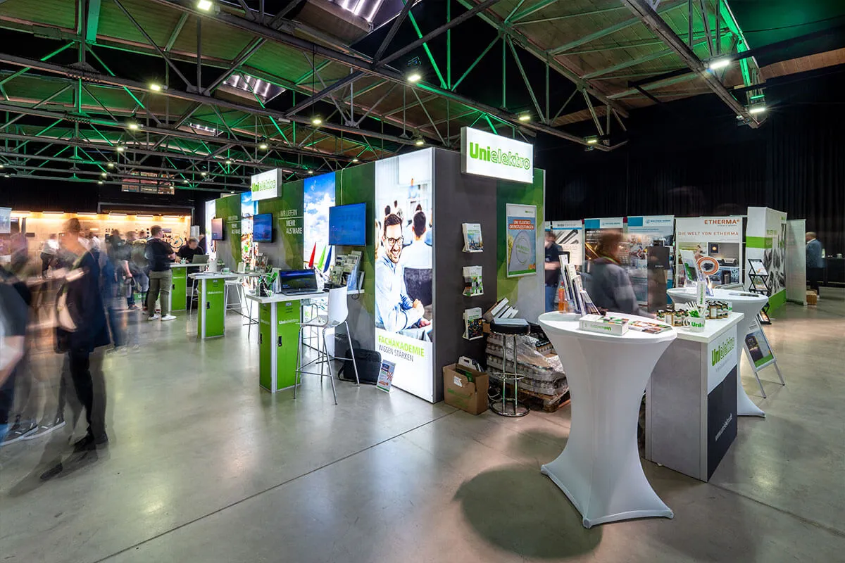 Messehalle mit Ausstellungsständen und grüner Beleuchtung