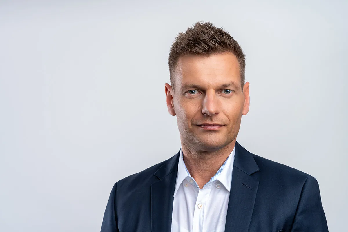 Headshot eines Mitarbeiters im dunklen Anzug vor hellgrauem Hintergrund