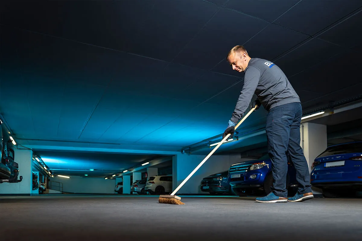 Mitarbeiter kehrt den Boden einer blau beleuchteten Tiefgarage