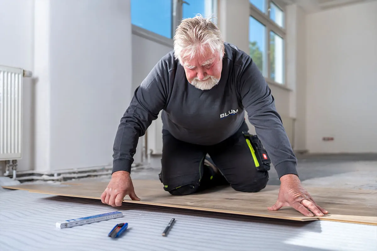 Handwerker verlegt Laminatdielen in einem leeren Raum