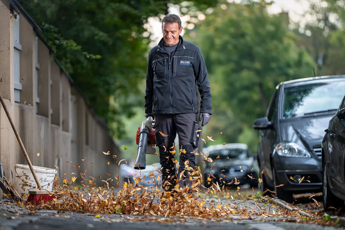 Mitarbeiter von Blum Immobiliendienste bläst Herbstlaub von einem Gehweg