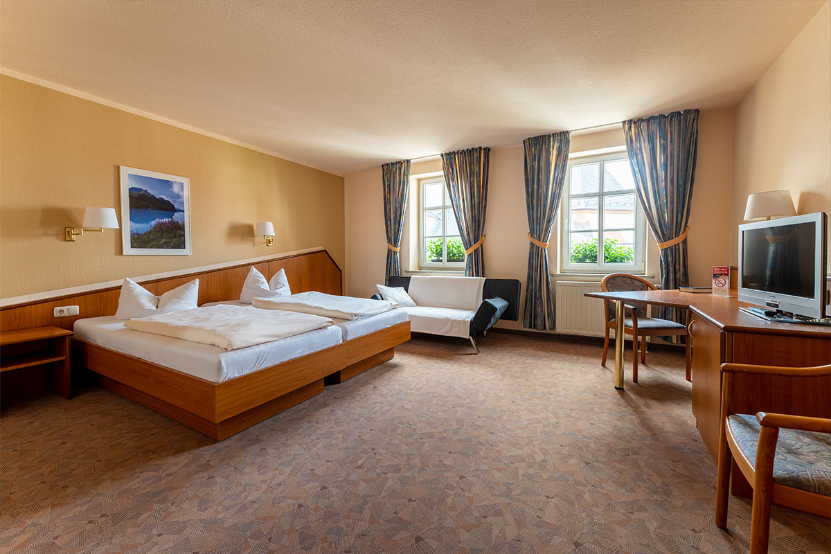 Doppelzimmer mit Bett, Sitzecke und Schreibtisch am Fenster