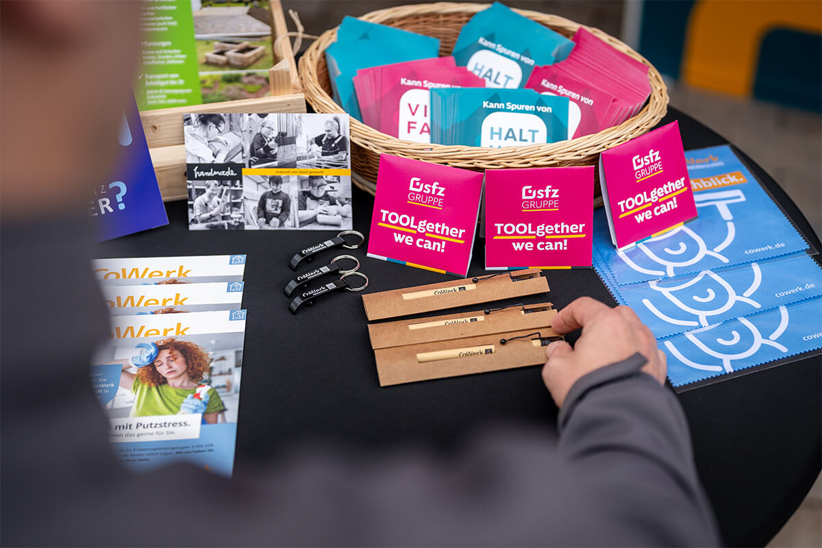 Give-aways der SFZ-Gruppe auf dem Stehtisch, eine Hand greift danach