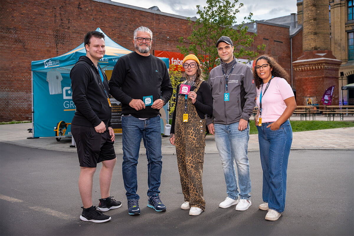 Fünf Standbetreuer im Gruppenbild vor der Backsteinkulisse des Festivalgeländes