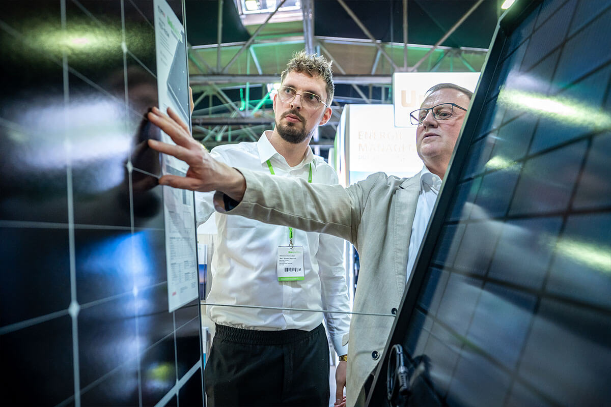 Zwei Besucher vergleichen Solarmodule am Stand, einer zeigt auf das Datenblatt